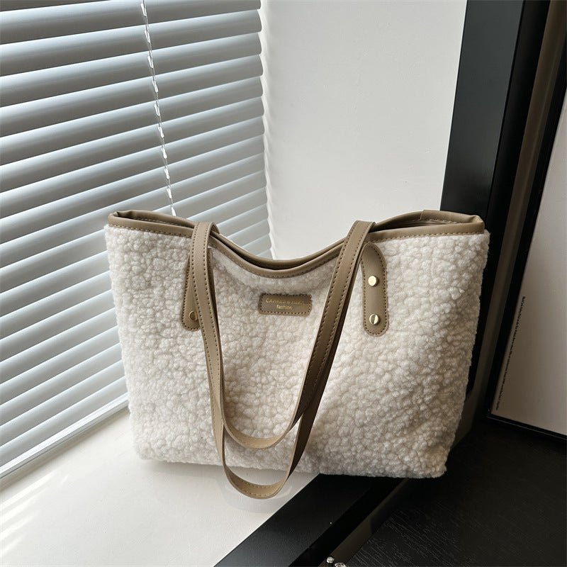 White textured handbag with brown strap and trim on a surface near a window with blinds.