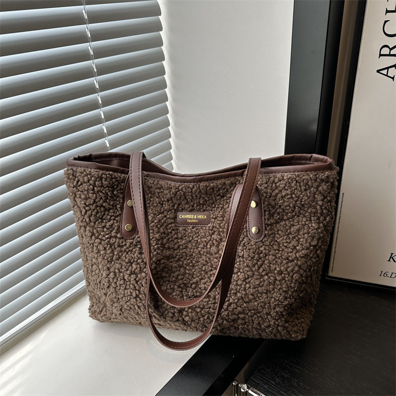 Brown textured handbag with leather straps on a surface near a window with blinds.